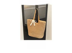 Detail of khaki straw tote with white lace bow and brown leather shoulder straps