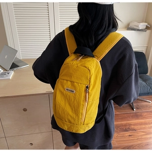 Detail of a bright yellow waterproof nylon backpack with zipper pockets on model