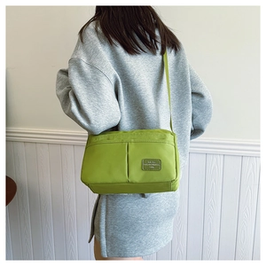 Detail of avocado green nylon crossbody bag with multi-pocket design and leather logo patch