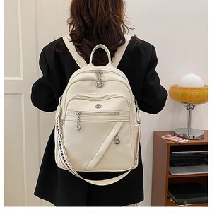 Dettaglio dello zaino minimalista in pelle crema con zip multistrato e tracolla intrecciata