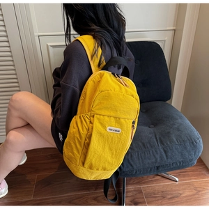 Bright yellow nylon backpack with brand label worn by model on a blue velvet chair