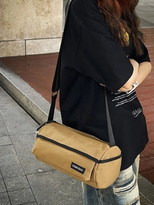 Sac bandoulière cylindrique en toile kaki avec sangle noire porté par un mannequin