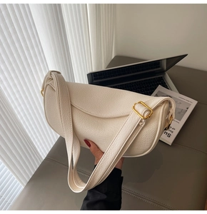 Detailed view of cream textured leather dumpling bag with elegant metal clasp and wide strap