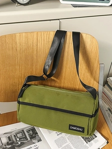 Sac cylindrique en nylon vert armée avec bandoulière noire réglable sur chaise en bois