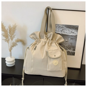 Detail view of cream tote bag showing drawstring closure and front zipper pocket texture