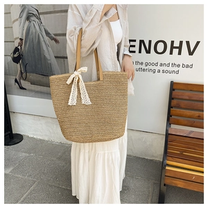 Detail view of woven straw tote bag with elegant white lace bow and faux leather handles