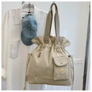 Detail of beige drawstring bucket bag featuring a zipper front pocket and relief logo
