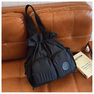 Detailed close-up of a black nylon drawstring tote bag with front pockets on a leather sofa