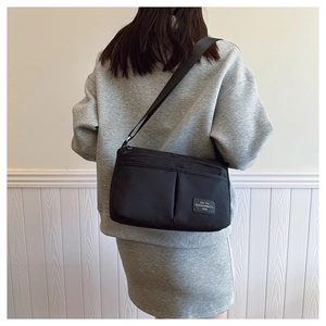 Close-up of black canvas crossbody bag featuring front zipper pocket and adjustable strap
