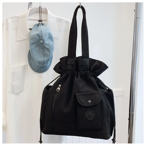 Detail of black canvas drawstring bucket bag featuring front pocket and woven straps