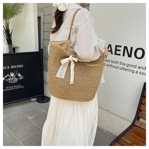 Detail of woven straw tote bag featuring white lace bow and brown leather straps