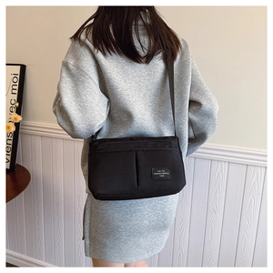 Detail of a black nylon crossbody bag with double front pockets and adjustable strap