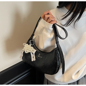 Close-up of black patent leather hobo bag with pearl lace bow charm and silver zipper