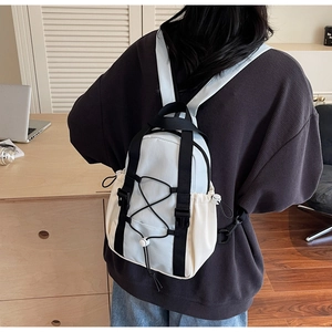 Back view of a model wearing a mini blue and beige backpack in a cozy indoor setting