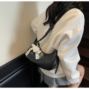 Detail of black patent leather crescent bag featuring a lace bow and pearl ornament