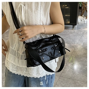 Detail of black pleated crossbody bag with bow ribbons and silver metal rivets