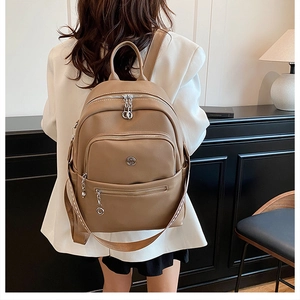Detail of khaki faux leather backpack with silver zippers and side strap on model