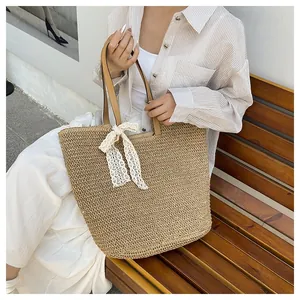 Detail of woven straw tote bag with brown leather handles and a white lace bow accent