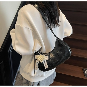 Detail of black glossy croissant bag with pearl bow charm on a model in minimalist setting