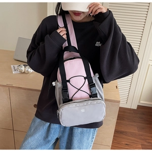 Detail of a pink and gray crossbody chest bag with adjustable straps and front bungee cord