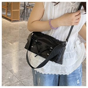 Detail of a black pleated crossbody bag with bow accents and studs on a female model
