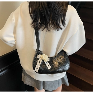 Detail of black semi-moon hobo bag in wrinkled glossy leather with pearl lace bow