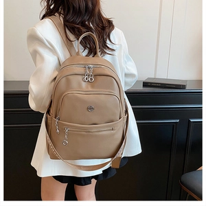 Detail view of khaki pebbled leather backpack with silver chain zippers and metal logo