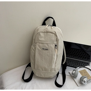 Detail shot of the beige nylon backpack with brand logo on a desk with a laptop