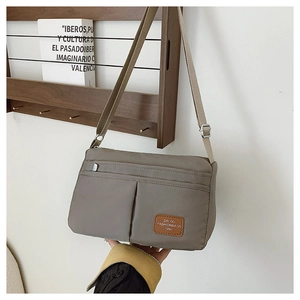 Detail of khaki nylon crossbody bag showing multiple pockets and leather logo patch