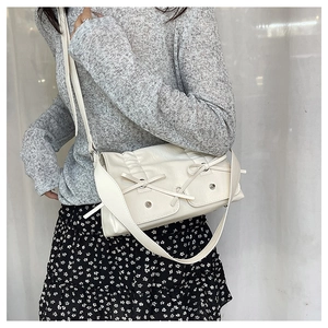 Detail of cream pleated leather shoulder bag with decorative bows and metal accents