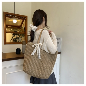 Detail of handwoven straw tote bag with delicate white lace bow and leather handles