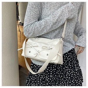 Close-up of cream rectangular shoulder bag with double bows and silver metal studs