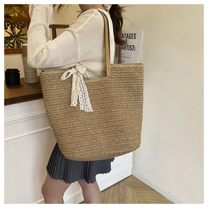 Detail of woven straw tote bag featuring leather handles and a white lace bow accent