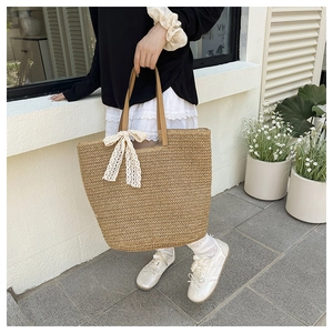 Close-up of woven straw tote bag featuring leather handles and a cream lace bow detail