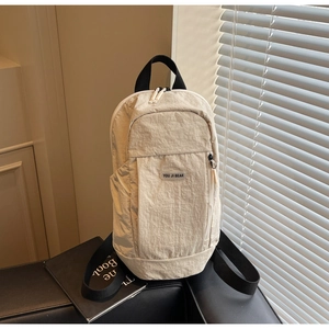 Detail of light beige nylon backpack featuring a logo patch and black fabric top handle