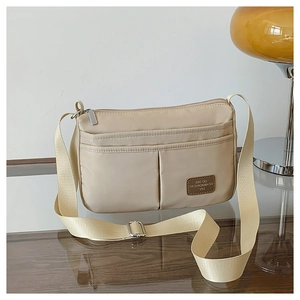 Detail of beige canvas crossbody bag showing multiple pockets and wide nylon strap