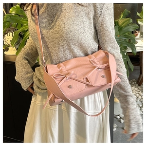 Pink crossbody bag detail featuring decorative bows and silver rivets on a square flap