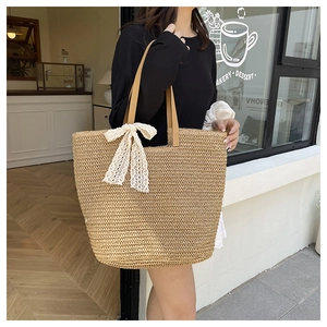 Detail of hand-woven straw tote with white lace bow and brown leather handles