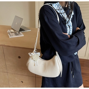 Close-up of white half-moon bag with elegant heart pearl and lace bow pendant detail
