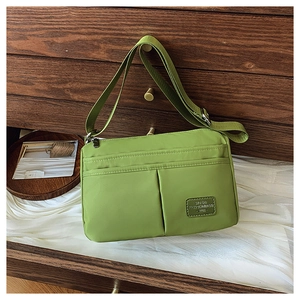 Detailed view of large green nylon crossbody bag with textured fabric and leather logo patch