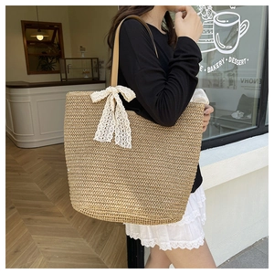 Detail of hand-woven straw tote bag with lace bow and leather shoulder strap