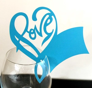 Close-up of bright blue heart-shaped Love laser-cut card placed on a wine glass rim