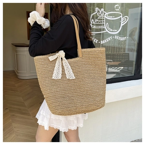 Detailed close-up of woven straw tote bag with lace bow decoration and brown straps