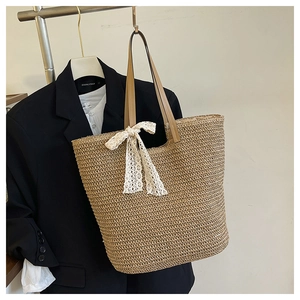 Detail of woven straw tote bag featuring a cream lace bow and leather handles on display