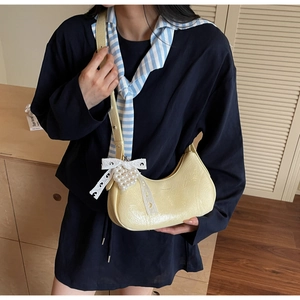 Close-up of pale yellow crescent bag with lace bow and heart-shaped pearl pendant