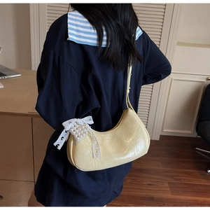 Detail of yellow patent leather hobo bag featuring lace bow and pearl heart charm
