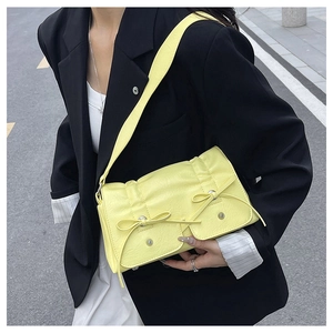 Detail of yellow pleated handbag with bow accents and side pockets on shoulder strap
