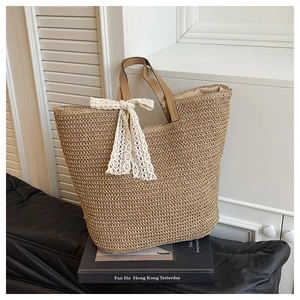 Detail of hand-woven straw tote bag with lace bow and leather handles on a decorative book