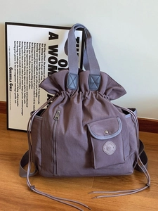 Purple pleated drawstring bucket bag with multiple pockets on warm wooden floor