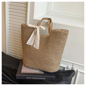 Detail of hand-woven straw tote bag featuring a white lace bow and brown leather handle